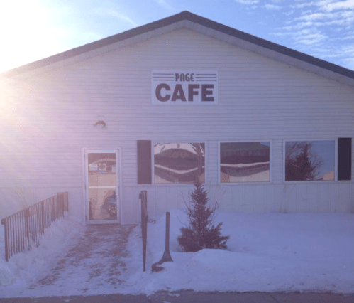 A white building with a sign reading "PAGE CAFE," surrounded by snow and a clear blue sky.