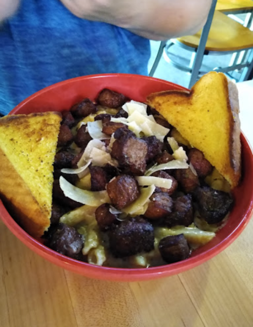 A red bowl filled with crispy diced meat, pasta, and topped with cheese, accompanied by two slices of toasted bread.