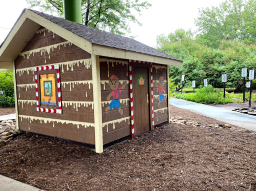 A whimsical gingerbread house structure with candy decorations, set in a garden area with walking paths.