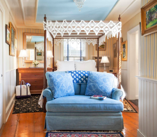 Cozy bedroom with a blue sofa, canopy bed, and decorative wall art, featuring warm lighting and a vintage feel.