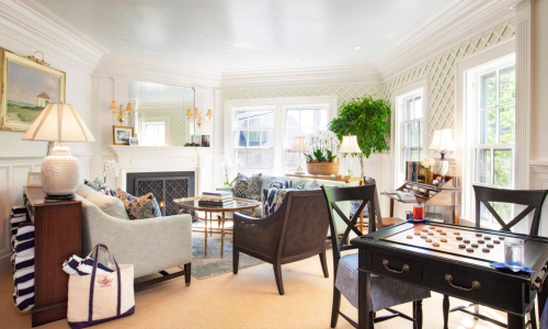 Cozy living room with a fireplace, comfortable seating, plants, and a checkers table, featuring bright natural light.