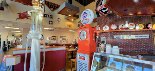 A retro diner interior featuring vintage gas pumps, memorabilia, and a cozy dining area with wooden tables.