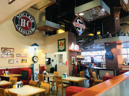 A retro diner interior with wooden tables, red booths, and vintage gas station signs on the walls.