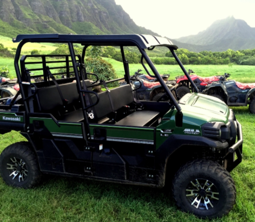 A green Kawasaki utility vehicle parked on grass with mountains in the background and other ATVs nearby.