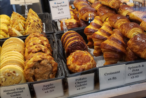 A display of assorted baked goods, including cookies, tarts, croissants, and galettes, with price tags.
