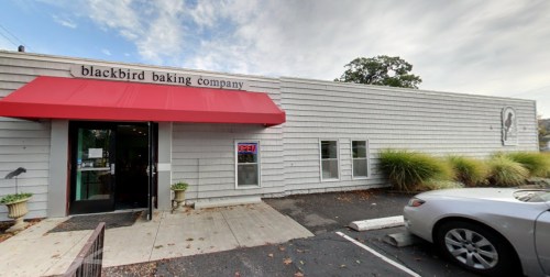 Exterior of Blackbird Baking Company with a red awning, open sign, and a parked car in front.