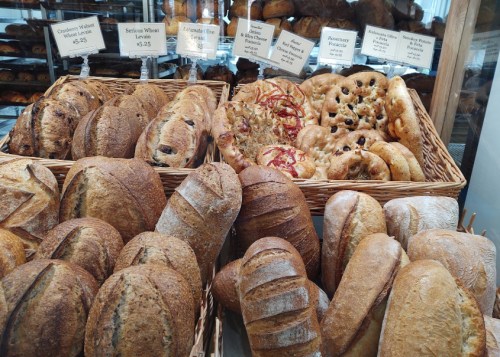 A variety of freshly baked breads in a display basket, including loaves and rolls with different textures and toppings.
