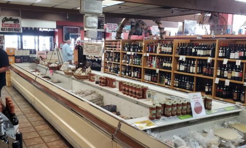 A grocery store interior featuring shelves of wine, jars of sauces, and a display of frozen goods.
