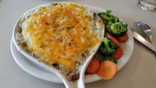 A creamy casserole topped with melted cheese, served with steamed broccoli and sliced carrots on the side.