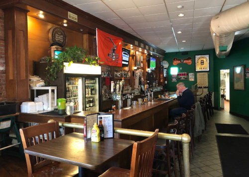 A cozy bar interior with wooden furniture, a long counter, and a Cleveland Browns flag on the wall.