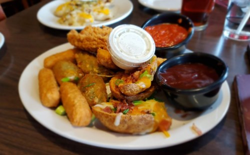 A plate of assorted appetizers including stuffed potato skins, fried pickles, and dipping sauces.