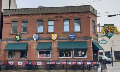 A brick building with green awnings, featuring colorful shields and a sign for "The Flag Iron" pub and restaurant.