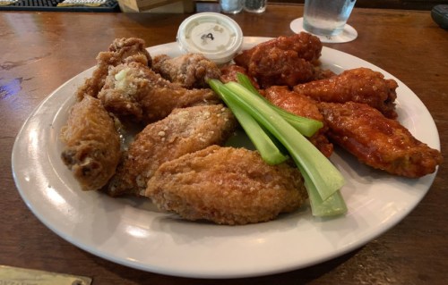 A plate of assorted chicken wings, including crispy and sauced varieties, served with celery sticks and a dipping sauce.