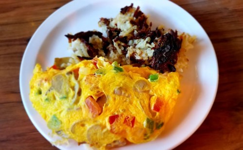 A plate with a colorful vegetable omelette and crispy hash browns on the side.
