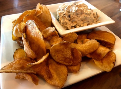 A plate of crispy potato chips served with a bowl of creamy dip.