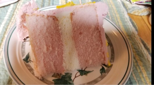 A slice of layered cake with pink and white sponge, served on a decorative plate with a floral design.