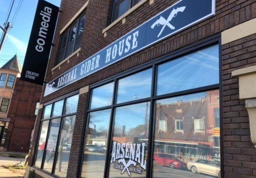 Exterior of Arsenal Cider House with large windows and signage, located in a brick building.