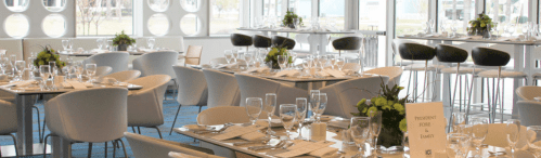 Elegant dining setup with tables set for a formal event, featuring glassware, cutlery, and floral centerpieces.