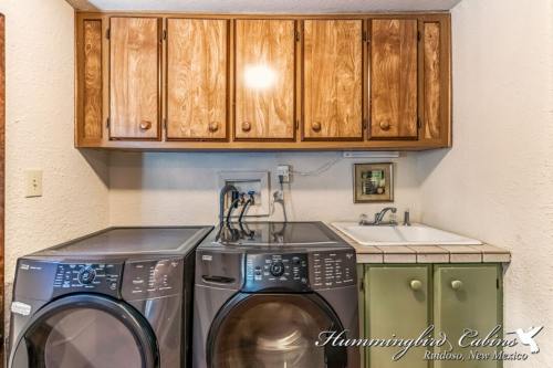 A laundry room featuring two washing machines, wooden cabinets above, and a small sink with green cabinetry.