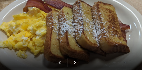 A plate with French toast dusted with powdered sugar, scrambled eggs, and crispy bacon.