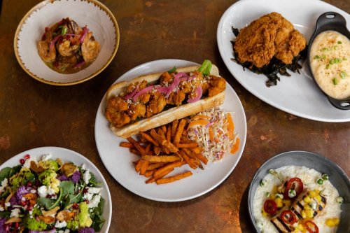 A spread of various dishes including fried chicken, shrimp, a sandwich, sweet potato fries, and a colorful salad.