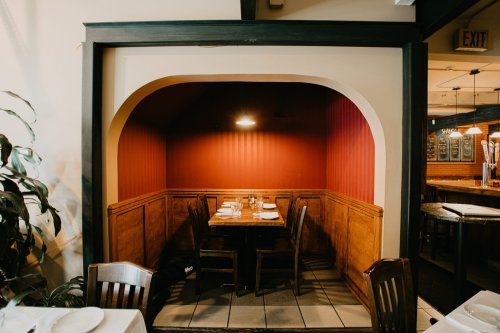 Cozy restaurant booth with wooden seating, a table set for dining, and warm red walls.