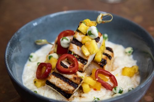 Grilled fish topped with mango salsa, red chili slices, and drizzled with a green sauce, served on a bed of creamy rice.