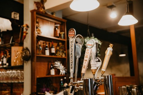 A close-up of beer taps in a bar, featuring various colorful tap handles against a warm, rustic background.