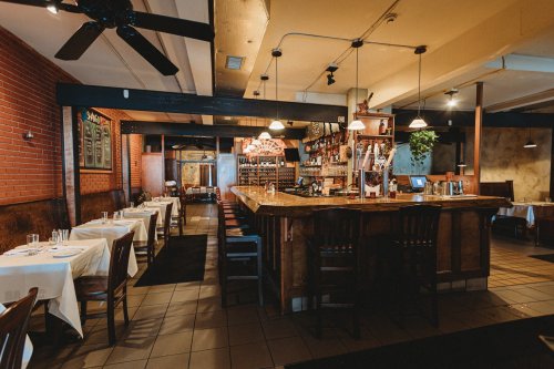 A cozy restaurant interior featuring a wooden bar, tables with white tablecloths, and a warm, inviting atmosphere.