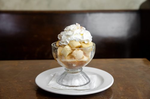 A glass dessert bowl filled with bananas, ice cream, and topped with whipped cream. Served on a white plate.