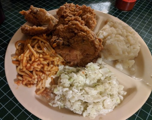A plate with fried chicken, coleslaw, mashed potatoes, and spaghetti.