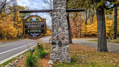 Sign for Sherwood Forest Lodge surrounded by colorful autumn trees and a paved road.