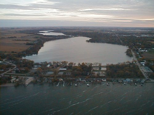 Aerial view of a large lake surrounded by trees and a small town, with boats docked along the shoreline.
