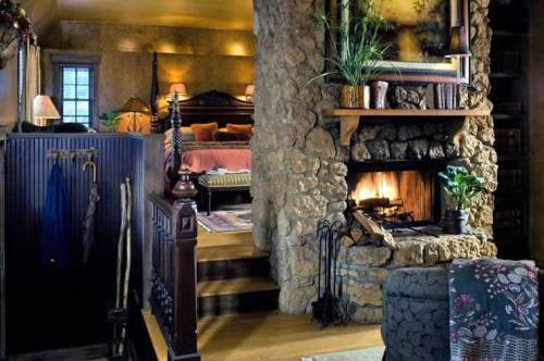 Cozy interior featuring a stone fireplace, wooden staircase, and warm lighting in a rustic bedroom setting.