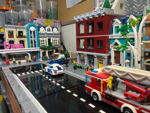 A colorful LEGO city scene featuring a diner, buildings, a police car, and a fire truck on a busy street.