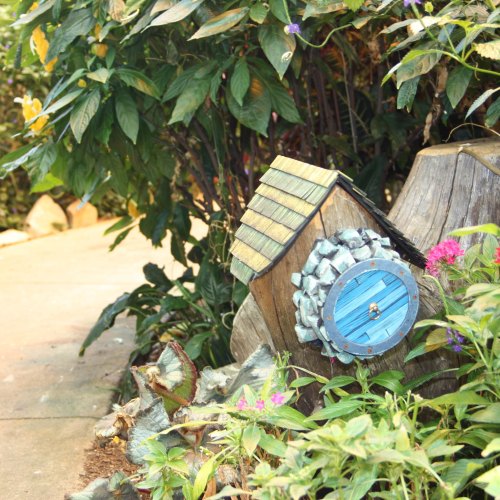 A whimsical wooden birdhouse with a blue door, nestled among lush green plants and colorful flowers.