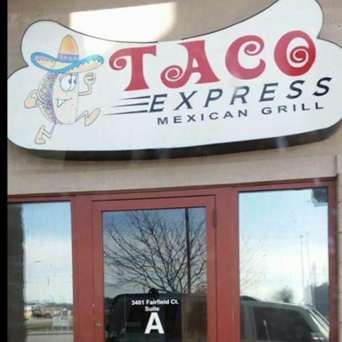 Sign for "Taco Express Mexican Grill" featuring a cartoon taco wearing a sombrero, with a door displaying the suite number.