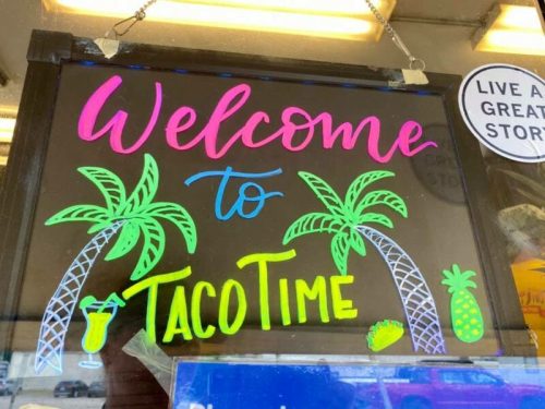 Colorful sign reading "Welcome to Taco Time" with palm trees, a taco, a drink, and a pineapple.