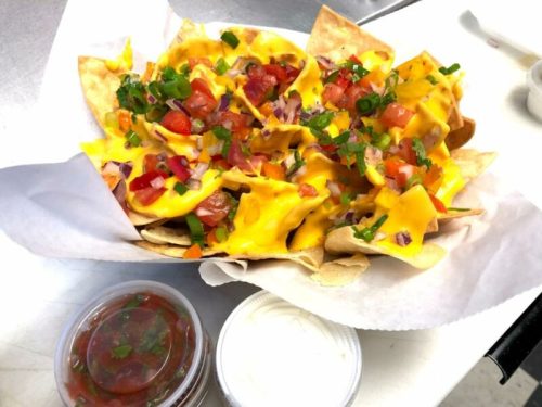 A plate of nachos topped with melted cheese, diced tomatoes, onions, and green onions, served with salsa and sour cream.