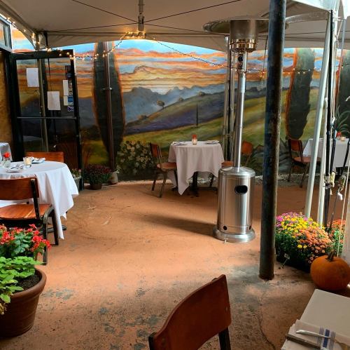 Cozy outdoor dining area with tables, colorful flowers, and a mural of a sunset landscape.