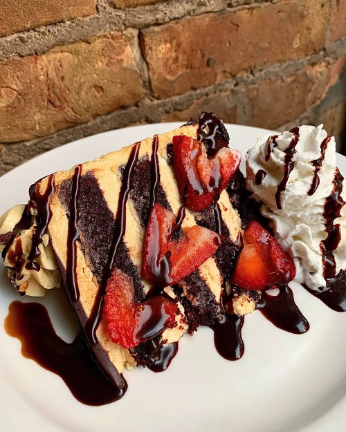 A slice of layered chocolate cake topped with strawberries, chocolate drizzle, and whipped cream on a white plate.