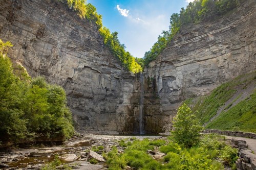 A stunning waterfall cascades down a rocky cliff surrounded by lush greenery and blue skies.