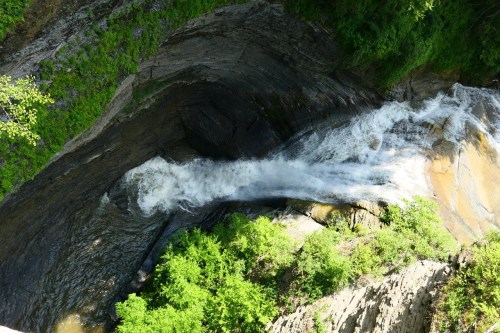 Aerial view of a waterfall cascading over rocky cliffs, surrounded by lush green foliage.