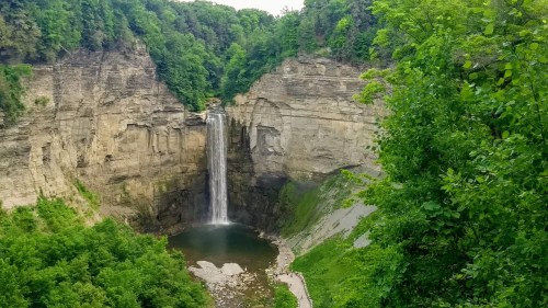 A scenic view of a waterfall cascading into a pool, surrounded by lush greenery and rocky cliffs.