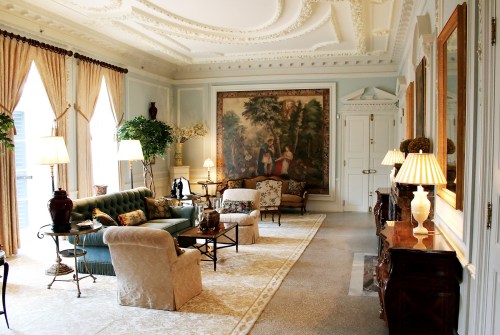 Elegant living room with ornate decor, plush seating, large windows, and a beautiful mural on the wall.