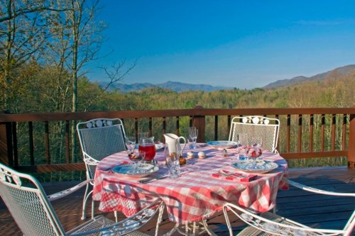 A scenic outdoor dining setup with a checkered tablecloth, drinks, and mountains in the background under a clear blue sky.
