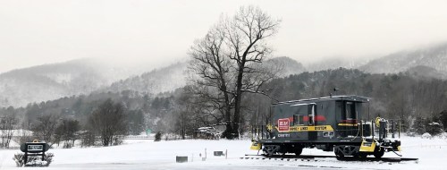 A snow-covered landscape features a vintage train car near a sign, with misty mountains in the background.