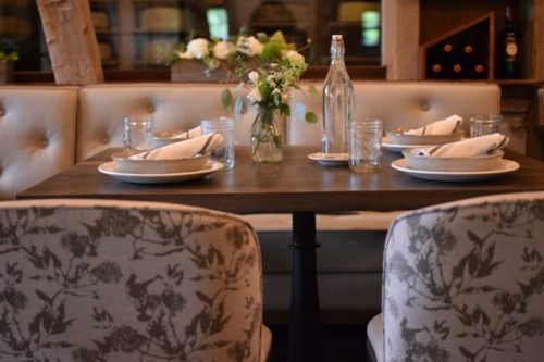 A cozy dining table set with plates, glasses, and a small flower vase in a warmly decorated restaurant.