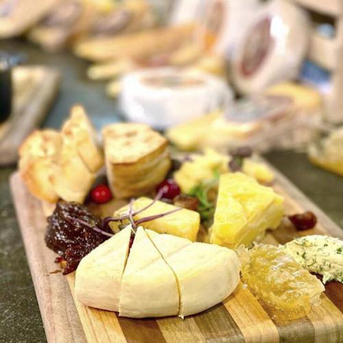 A wooden cheese board featuring various cheeses, fruits, and accompaniments like jams and herbs.