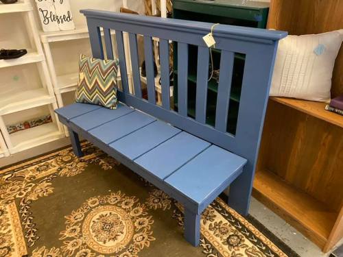 A blue wooden bench with a patterned pillow, placed on a decorative rug in a cozy interior setting.